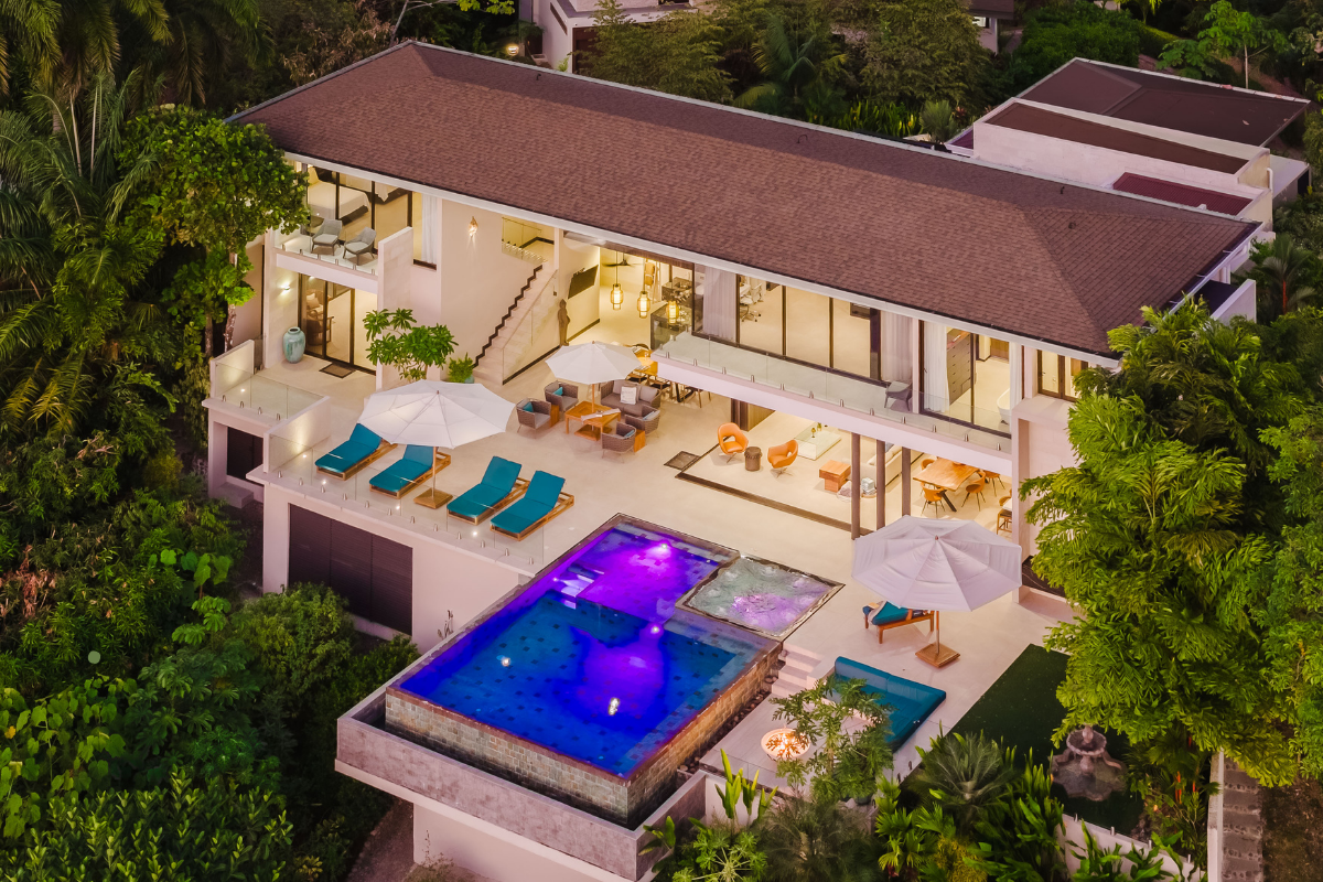 Luxury multi-story house at night featuring illuminated glass walls and a spacious terrace.