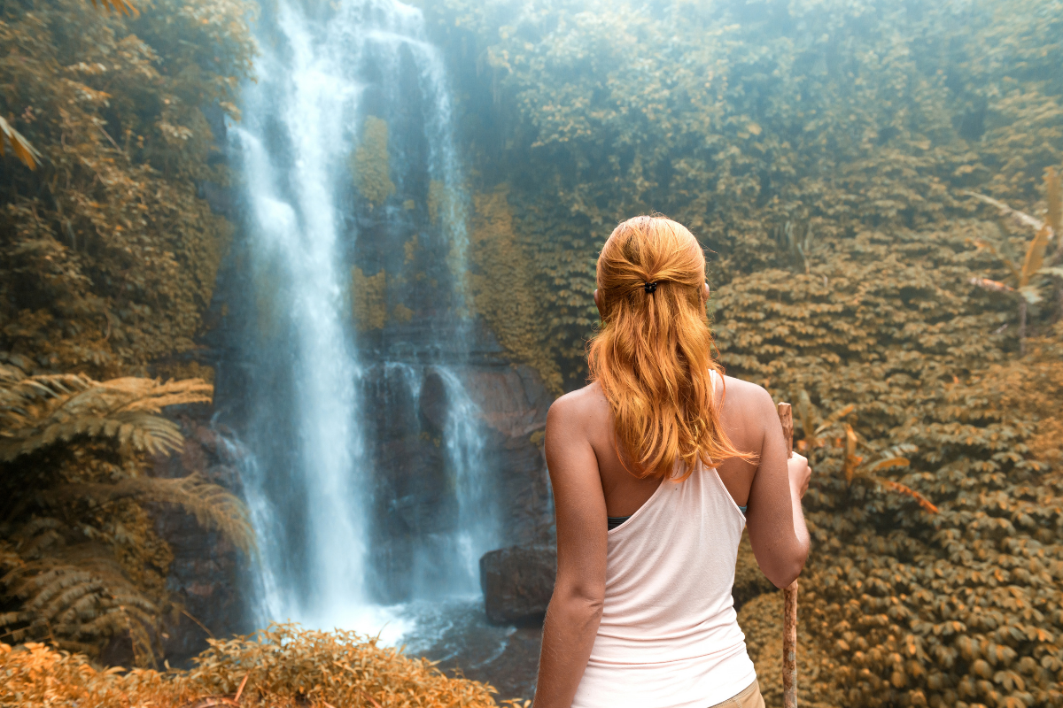A guy standing in a river with his arms upwards receiving a huge waterfall.