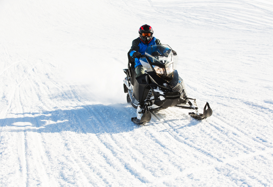 Person snowmobiling in an open, snowy spot.