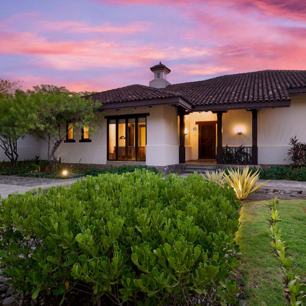 Elegant colonial-style villa with terracotta roof and landscaped gardens under a colorful Costa Rica sunset.