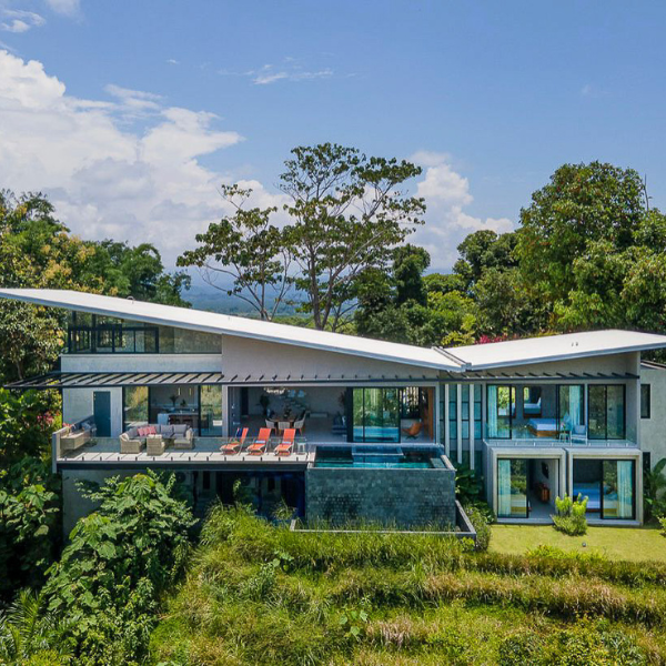 A modern hillside home with a dramatic slanted roof, clean lines, concrete accents, and tropical landscaping surrounding the entrance.