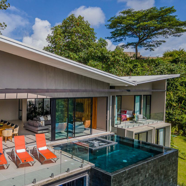 A luxury villa with a large ocean-view terrace, infinity-edge pool, and sleek overhang structure opening to outdoor lounge chairs and seating.