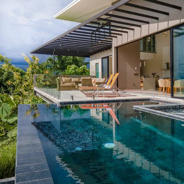A terrace-level infinity pool reflecting the home’s modern architecture, with lounge chairs and forest views in the background.