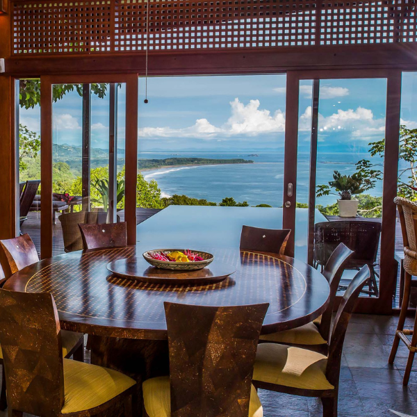 Elegant dining room with round wooden table, panoramic glass doors, offering breathtaking views of the Whales Tail and coastline.