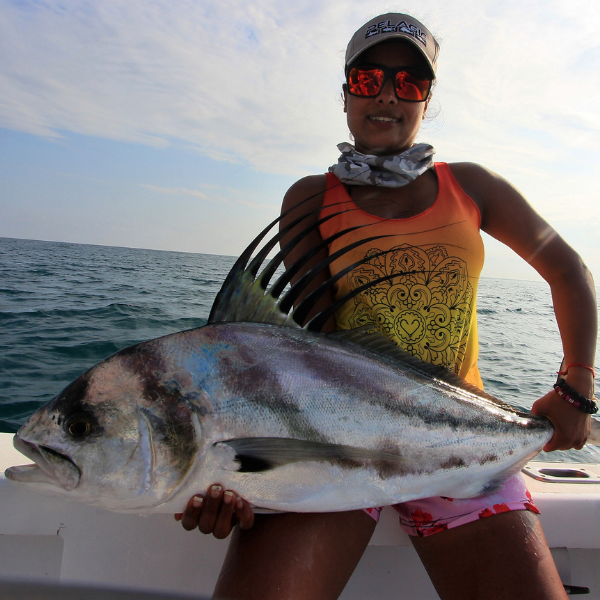 ALT A woman holding a large roosterfish on a boat in the ocean.
