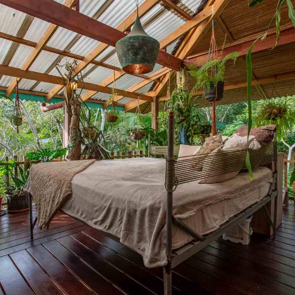 Open air bedroom with canopy bed, wood floors, and tropical jungle views