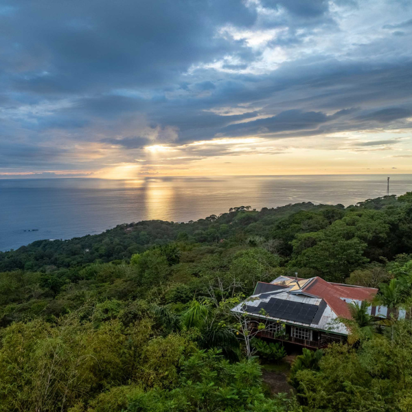 Aerial view of oceanfront jungle home with solar panels and sunset over the Pacific