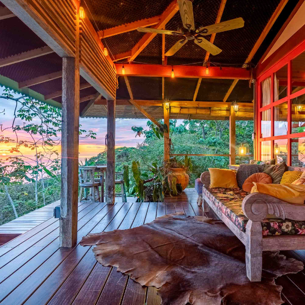 Covered ocean view terrace with wood deck, lounge seating, and sunset view