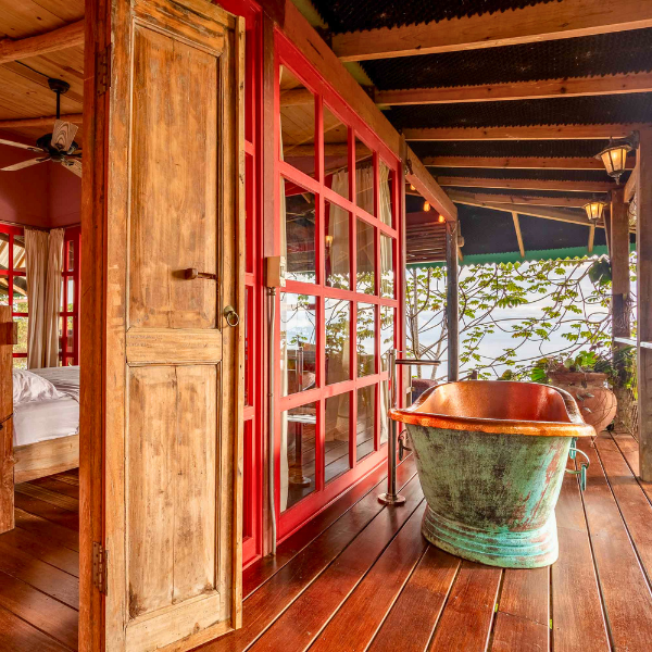 Outdoor copper bathtub on wood deck beside red framed glass doors