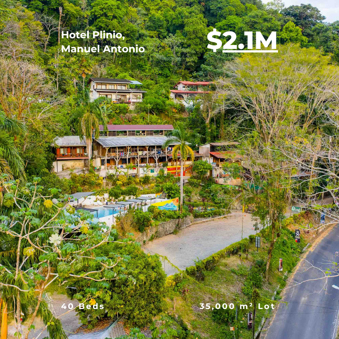 Hillside hotel property surrounded by dense jungle, multiple buildings, and a large parking area.