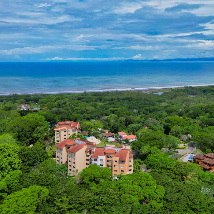 Aerial view of Nativa Resort in Jacó showing buildings surrounded by dense jungle with ocean and beach in the background.