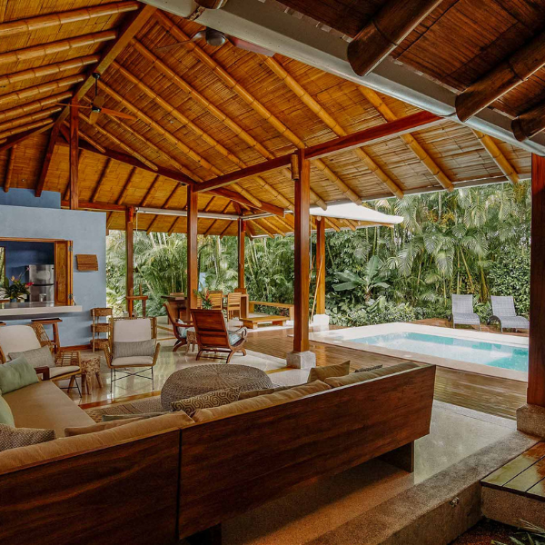 Open-air living area with wooden ceiling, modern furniture, and private pool surrounded by lush jungle in Santa Teresa.