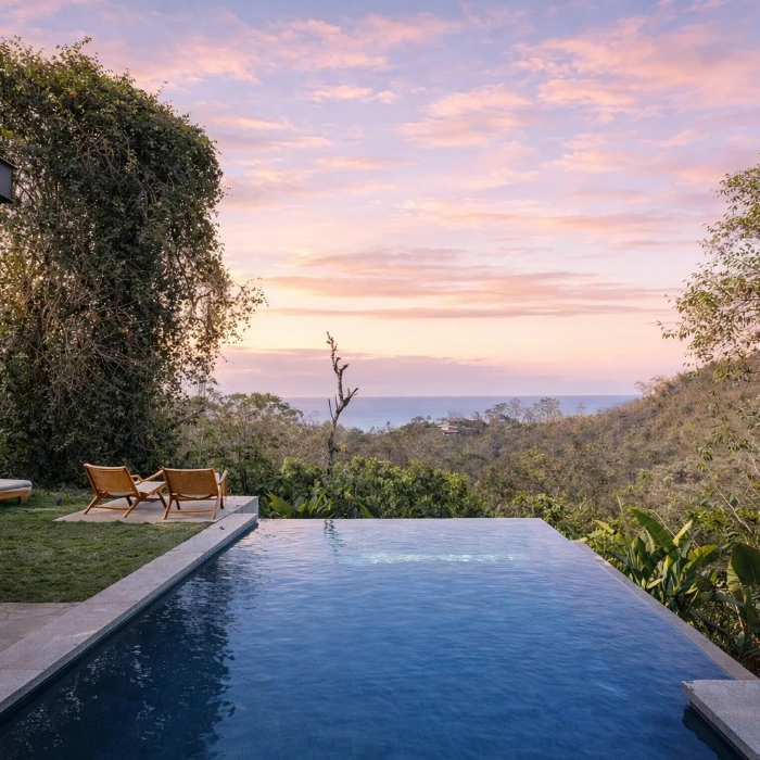 Infinity-edge swimming pool overlooking tropical jungle and ocean views during a pastel sunset in Santa Teresa, Costa Rica.