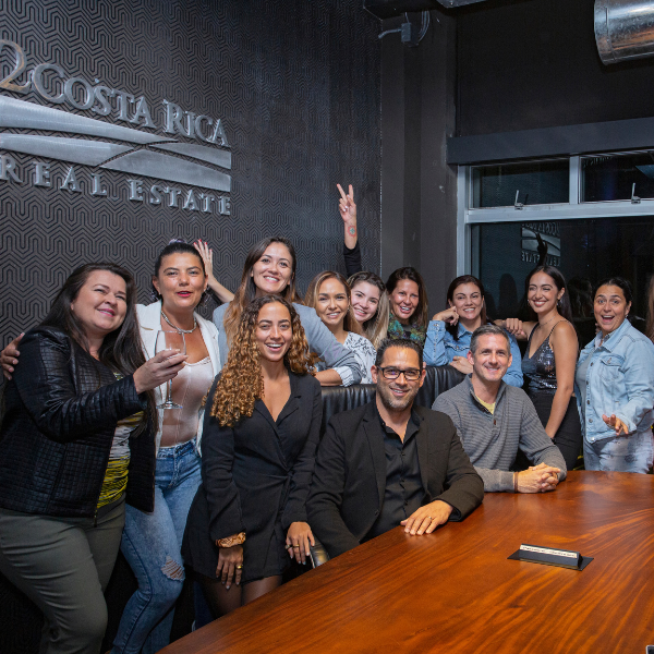 Team group photo inside a modern real estate office conference room, with staff members posing together around a wooden meeting table.