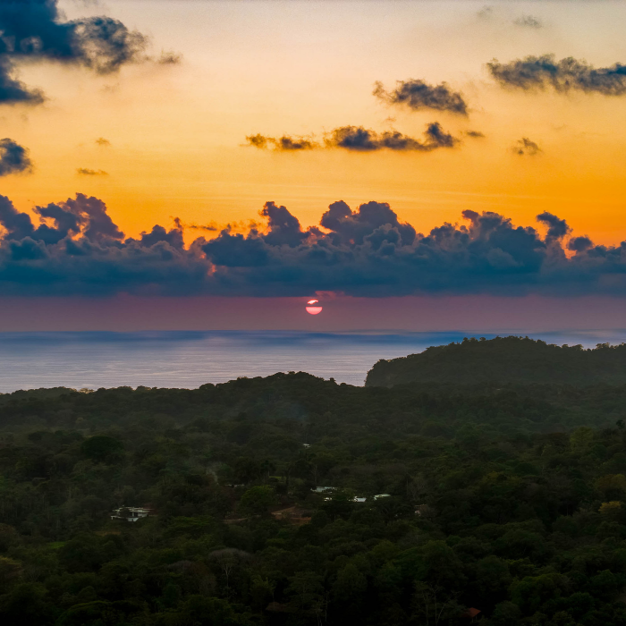 ocean sunset view above rolling jungle-covered hills, featuring vibrant clouds and serene Pacific coastline scenery.