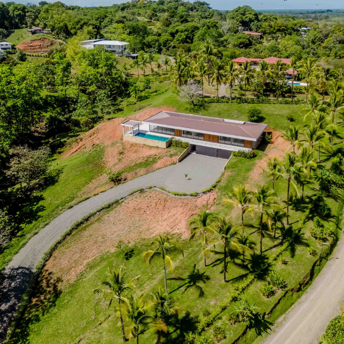 Aerial view of a lush tropical countryside community with rolling green hills, private estates, winding roads, and mountain ranges in the background.