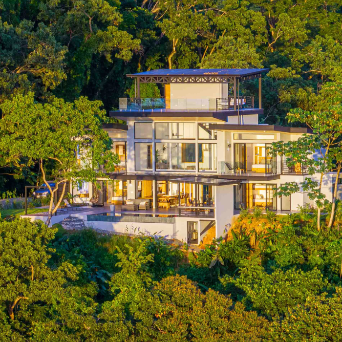 Modern multi-level luxury home surrounded by dense tropical jungle with large glass windows and multiple outdoor terraces.