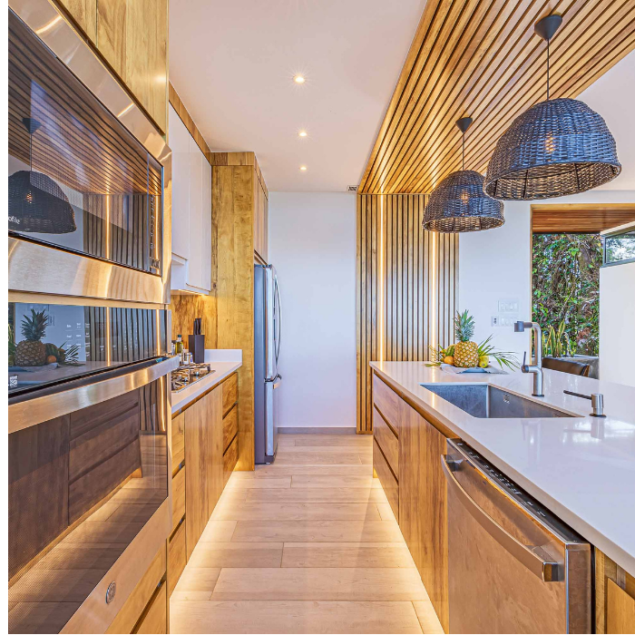 Modern wood-accent kitchen with white countertops, pendant lighting, and built-in appliances.
