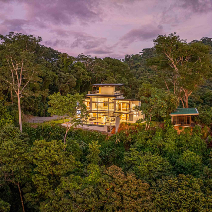 Luxury hillside home with infinity pool overlooking the ocean and tropical forest at sunset.