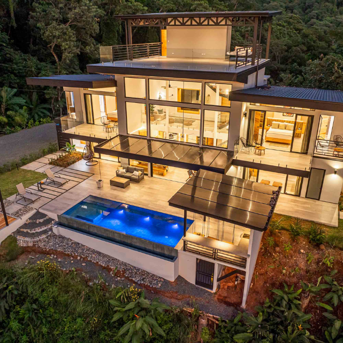 Aerial top down view of a modern hillside home with pool surrounded by dense greenery.