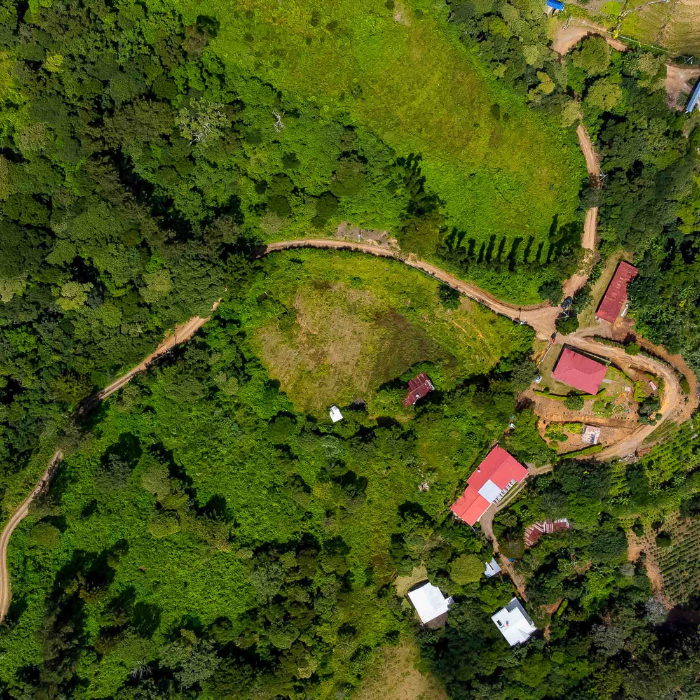Aerial view of a rural tropical property surrounded by dense greenery, winding dirt roads, and scattered homes.