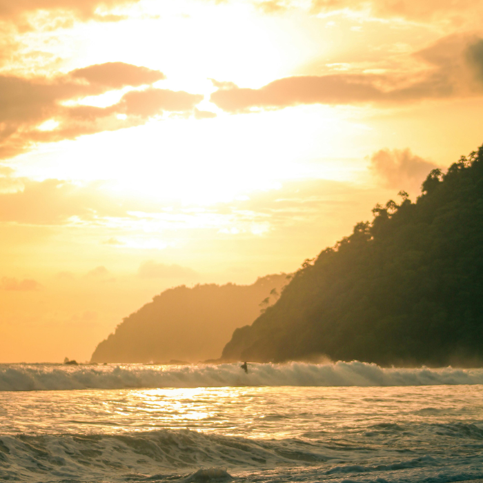 Ocean waves at sunset with a rocky coastline and warm golden light reflecting on the water.