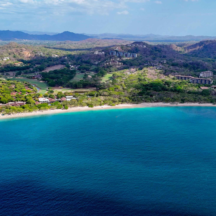 Aerial panoramic view of Flamingo Bay showing turquoise ocean, sandy beach and luxury hillside resort developments in Guanacaste Costa Rica