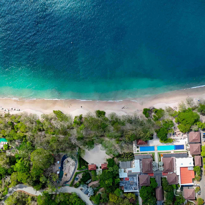 Top-down drone view of Flamingo beachfront with private pool estates, tropical tree canopy and pristine Pacific coastline