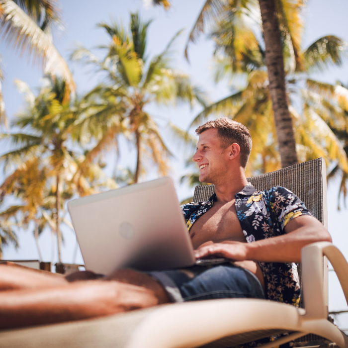 Man relaxing on a lounge chair with a laptop under tropical palm trees at a beachside resort in Costa Rica.
